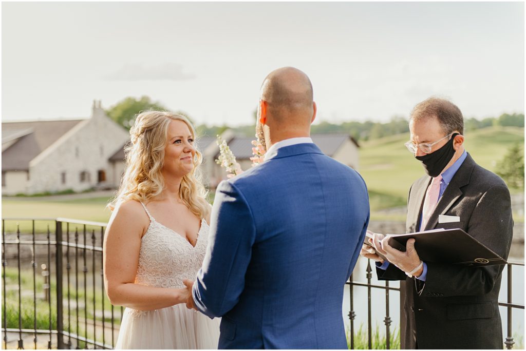 the bride smiling at her groom as they read their vows to each other on a balcony at Mistwood in Romeoville during sunset