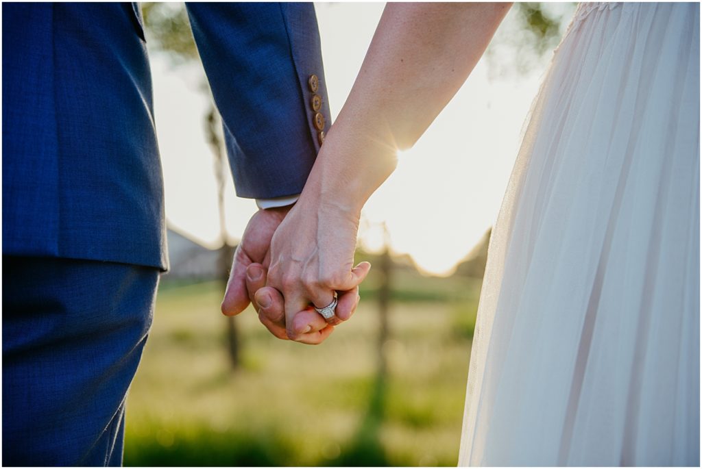 a bride and groom holding hands with the main focus on her ring with the setting sun in the background