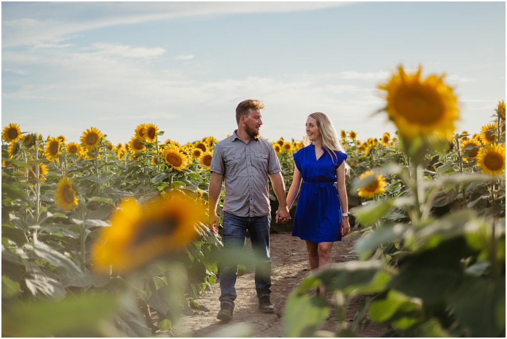 a husband and wife walking together down a old path during their Sunflower Field Engagement