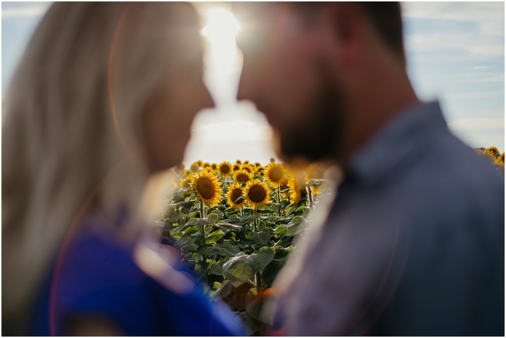 a couple standing with their heads together with a field of sunflowers behind them during their engagement session