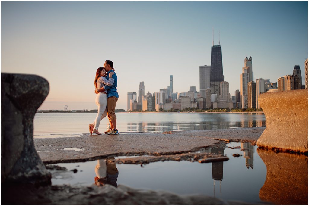 an engaged couple hugging at the Chicago Lakefront at sunrise while being photographed by one of the Chicago engagement photographers