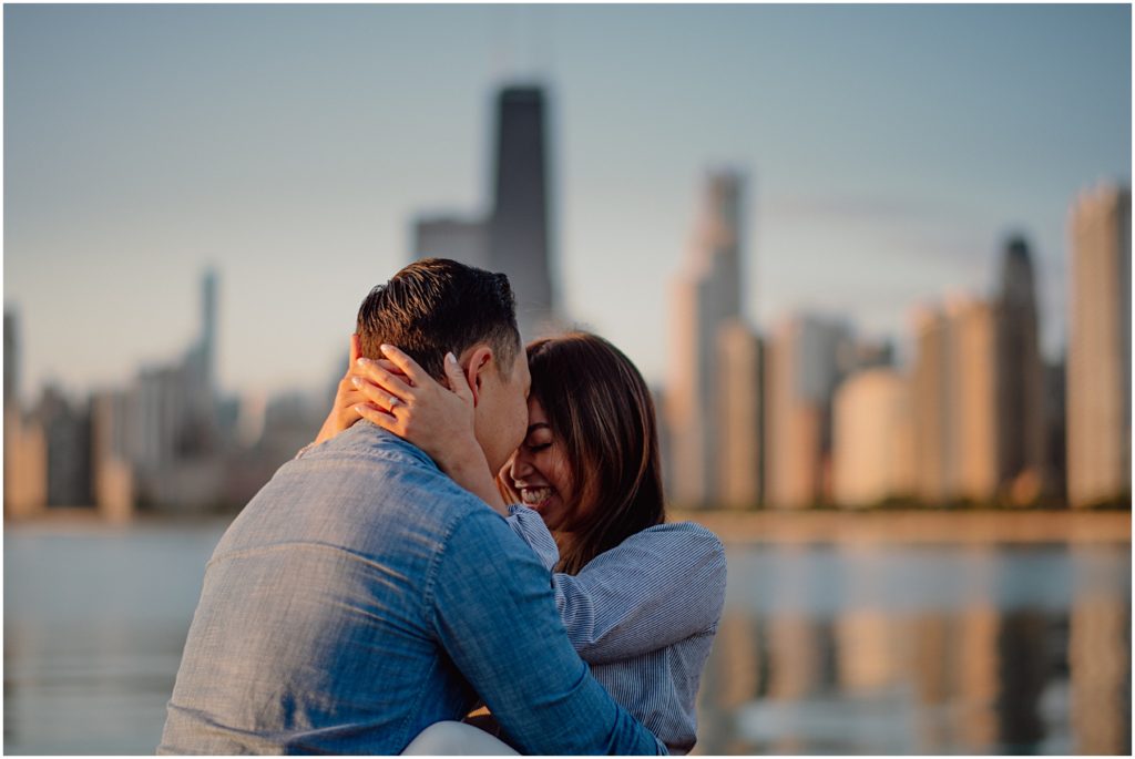 after choosing a photographer from the group of Chicago engagement photographers, a groom kisses his brides head as they sit together at the Chicago Lakefront at sunrise