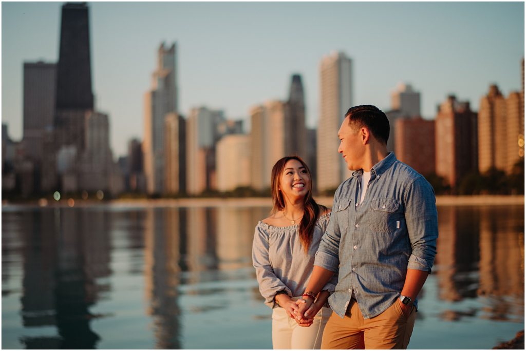 an engaged couple walking in front of the golden Chicago Skyline at their North Avenue Beach sunrise engagement session