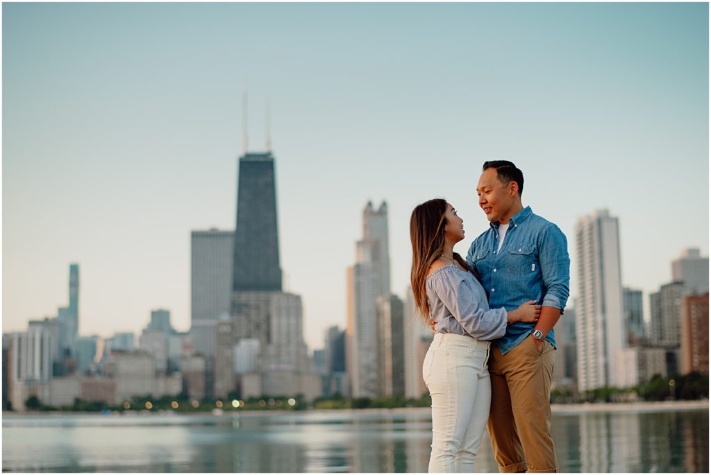 an engaged couple hugging each other in front of the Chicago Skyline at sunrise