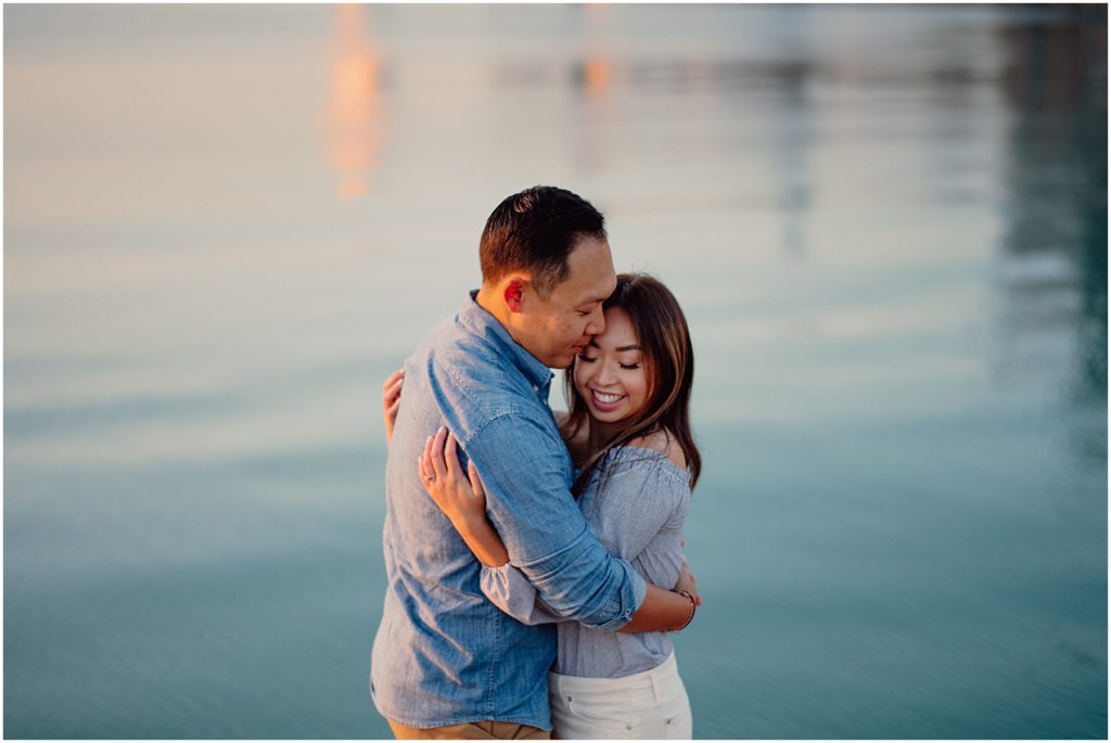a newly engaged couple hugging in front of pastel blue water after meeting a photographer from the Chicago engagement photographers