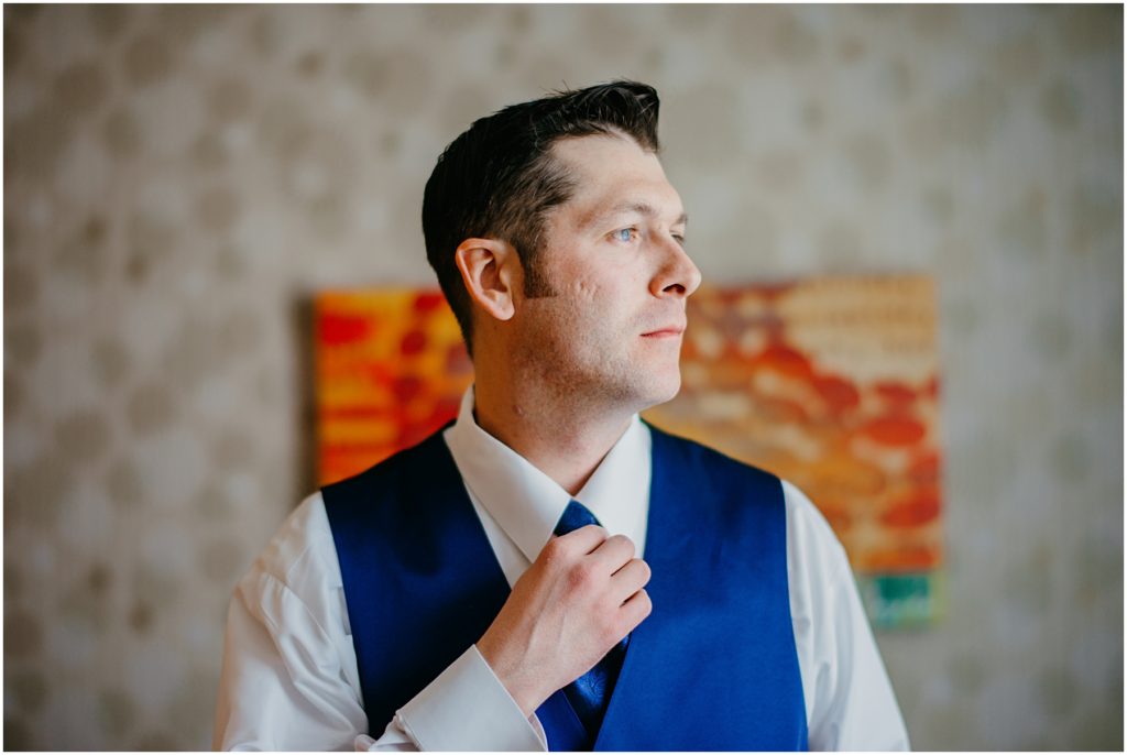 the groom adjusting his tie as he gets ready before his wedding in a colorful hotel room