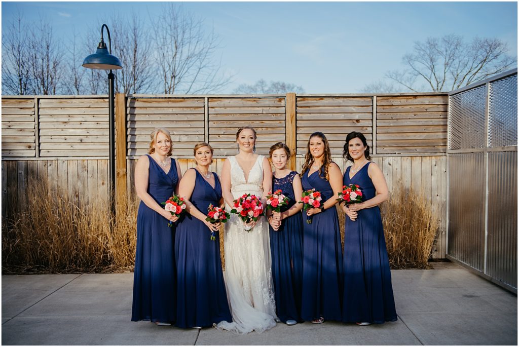 a bride with her bridesmaids wearing blue dresses at a warehouse wedding at sunset