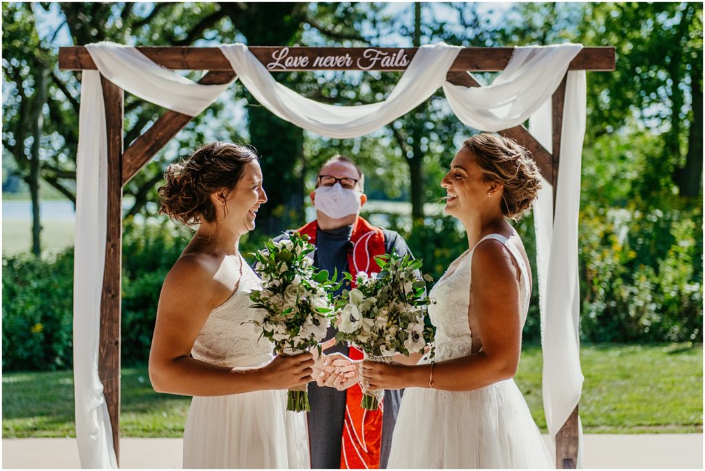 two brides laughing as they hold hands during their outdoor intimate wedding