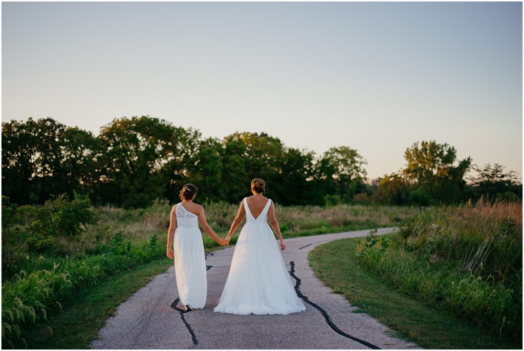 two brides walking down a pathway at sunset