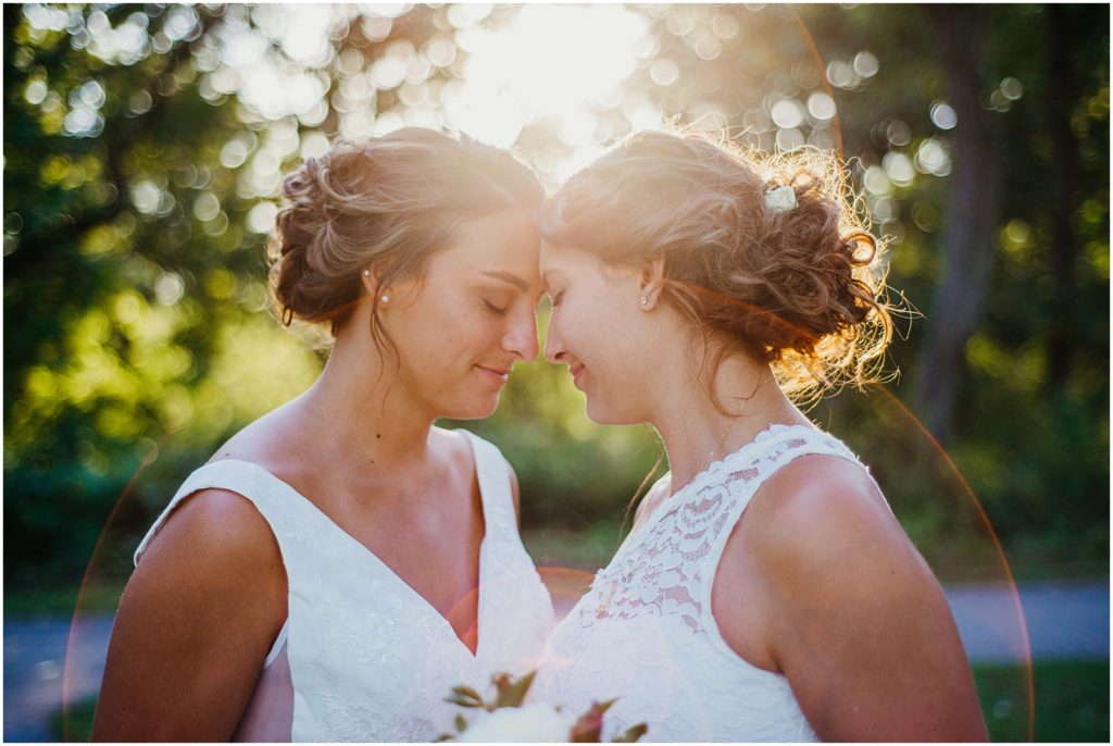 two brides standing with their heads together as the sun sets in the background at their intimate wedding